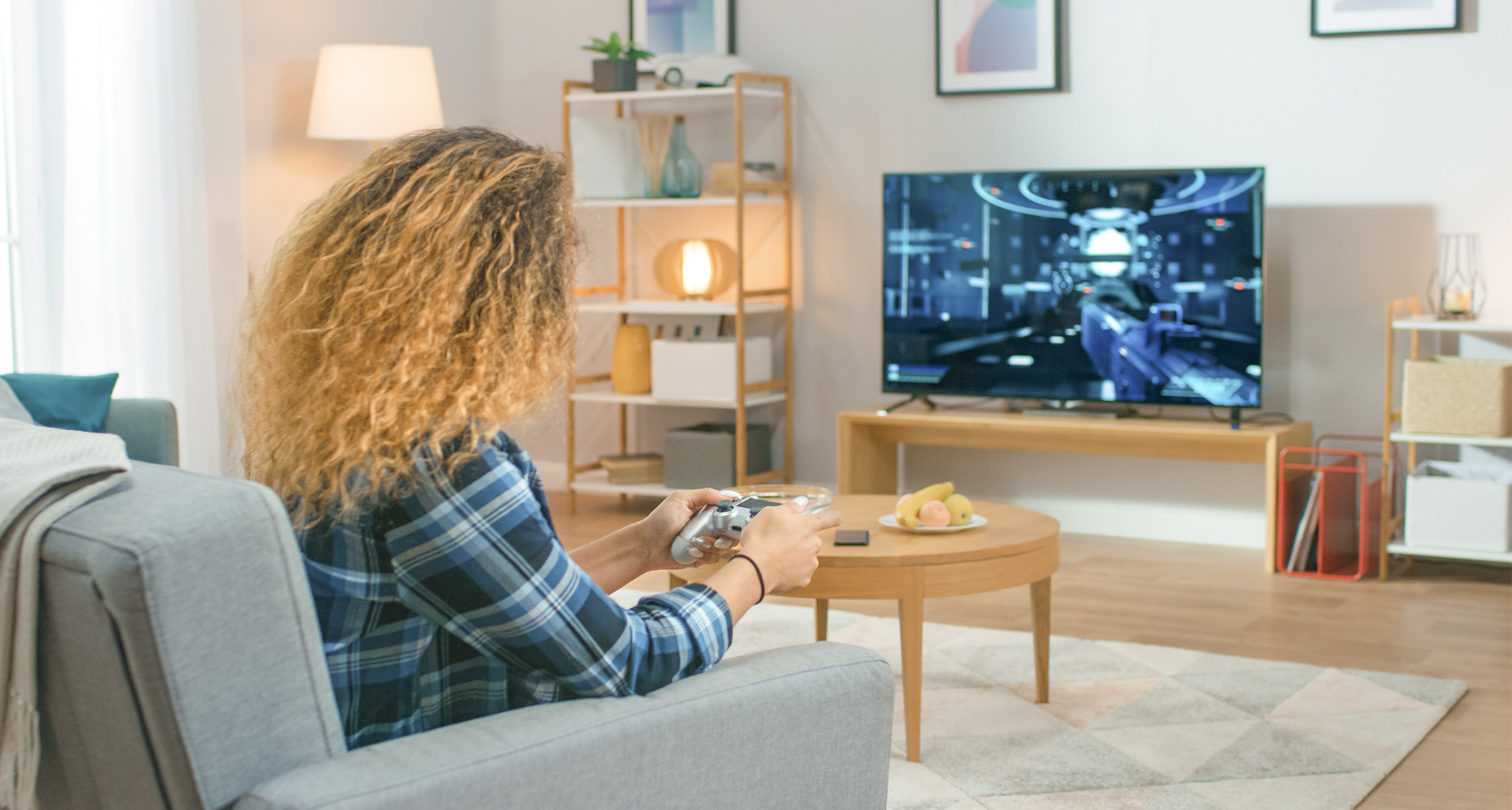 osoba z długimi kręconymi włosami w salonie grająca w gry wideo na telewizorze